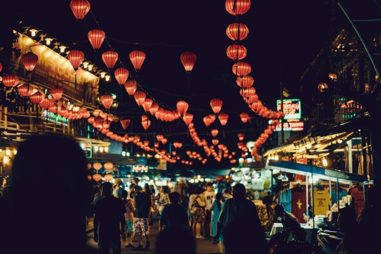 Visitors walking among market stalls beneath colorful hanging lanterns, reflecting travel and cultural exchange
